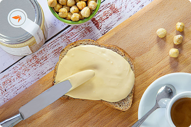 Pane a fette con sopra la crema di nocciola bianca e un cappuccino per colazione